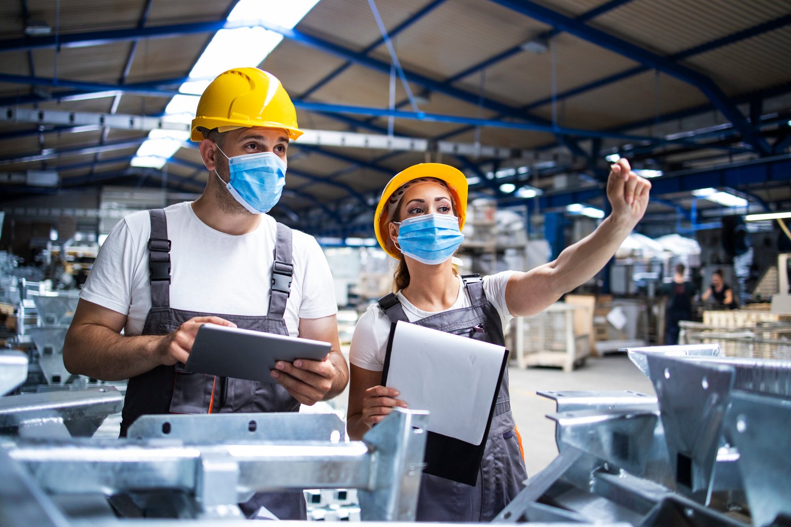 factory workers with face masks protected against corona virus doing quality control of production in factory.